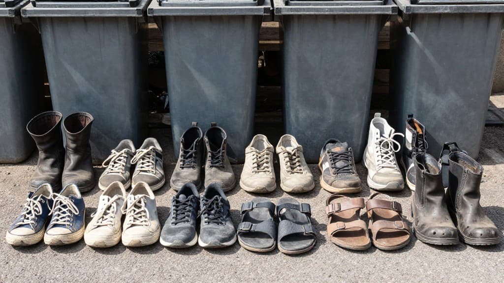 Verschiedene alte Schuhe sortiert nach Zustand und Art - Sportschuhe, Stiefel, Sandalen und kaputte Schuhe zur Entsorgung bereit