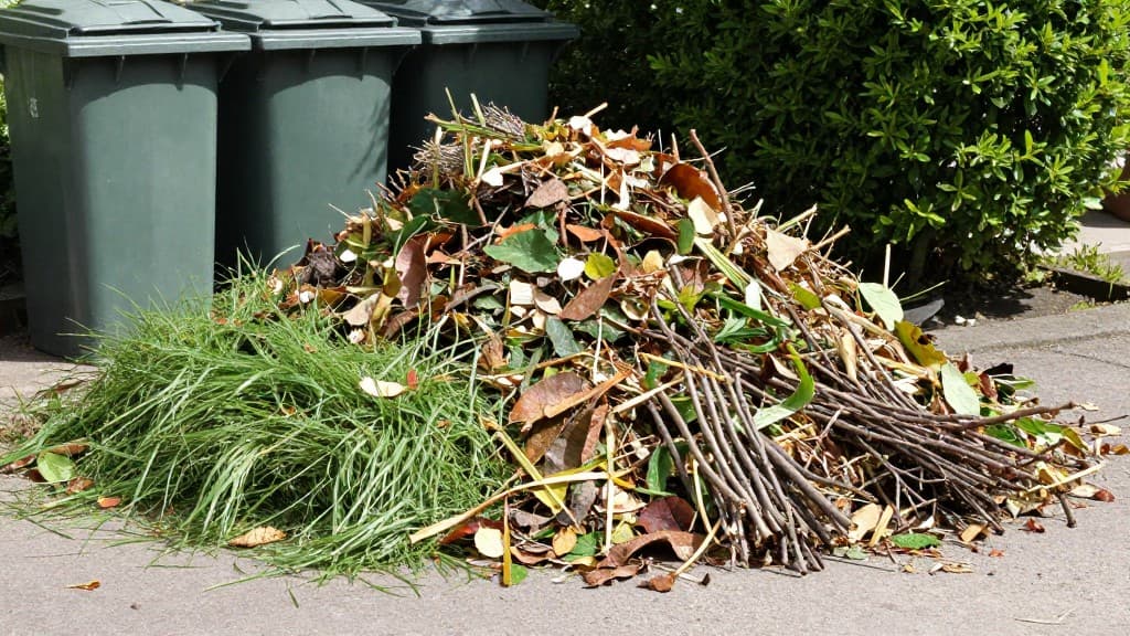 Verschiedene Gartenabfälle wie Rasenschnitt, Laub, Äste und Heckenschnitt, die für die Biotonne vorbereitet werden